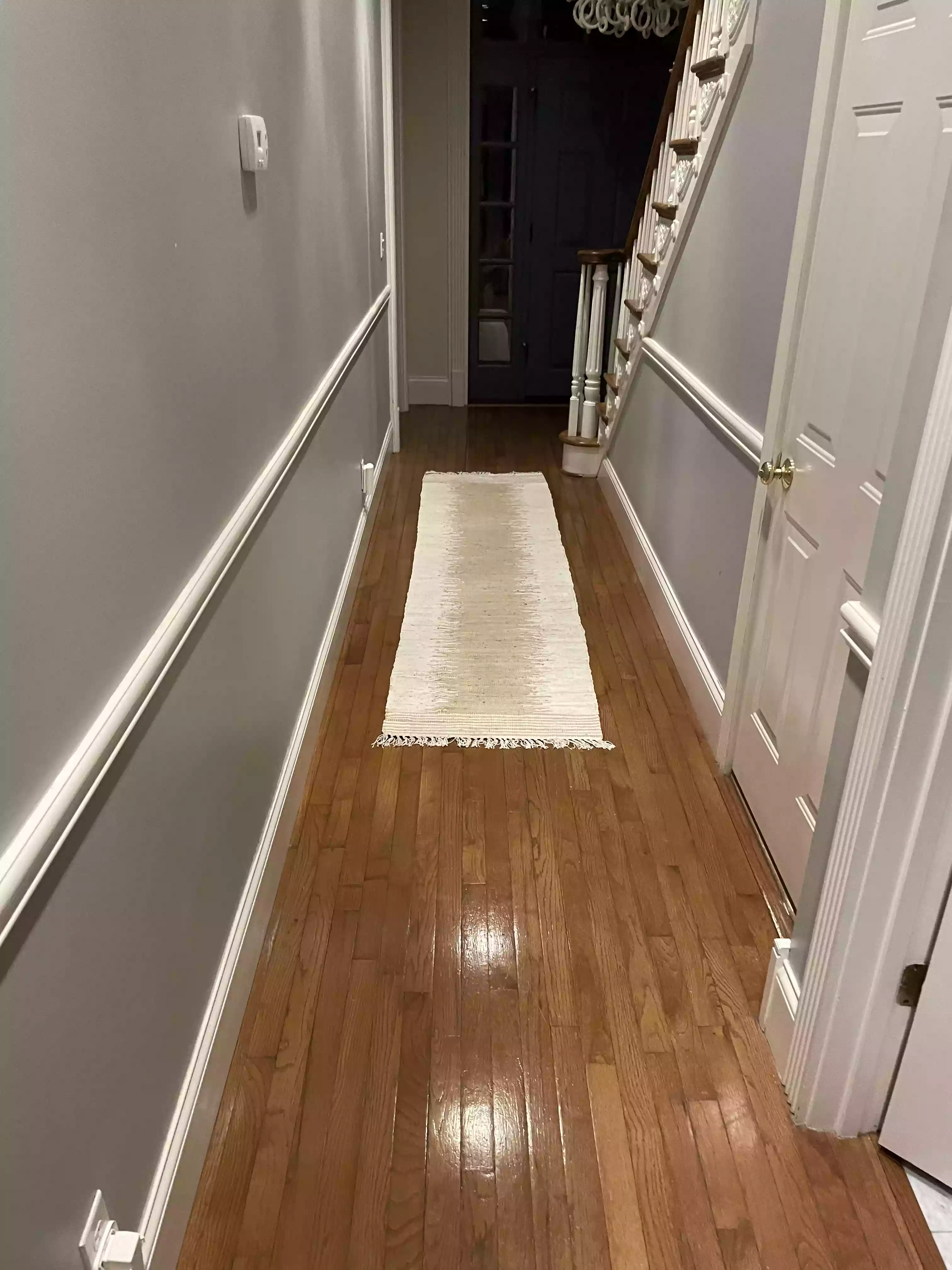 a medium-length hallway that has clean and shiny hardwood floors and features a beige and white runner
