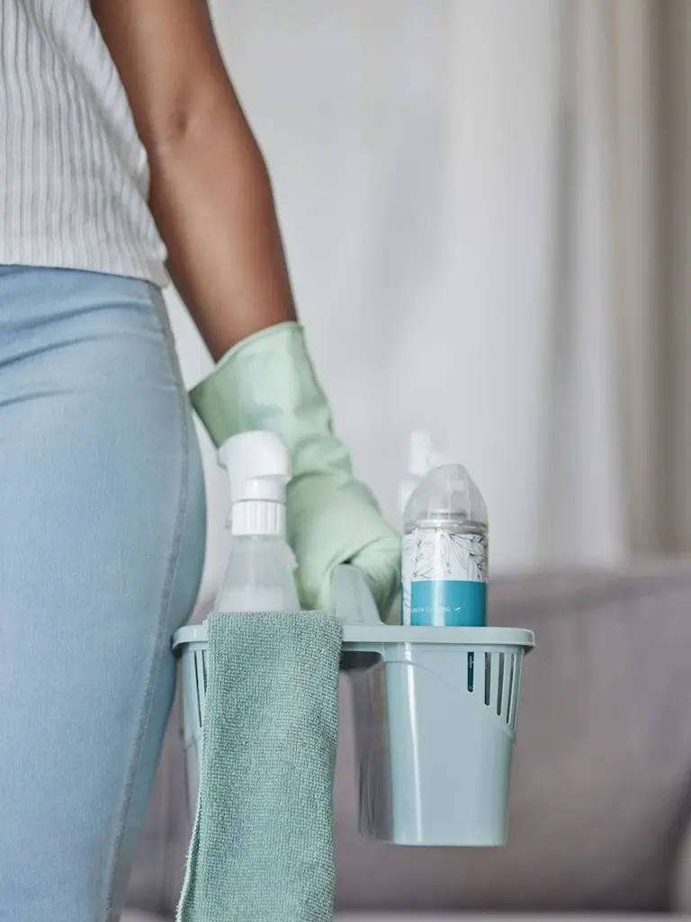 Woman holding a cleaning basket with supplies like spray bottles and sponges.